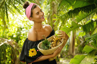 Happy young woman with a basket full of exotic fruits in the tropical garden